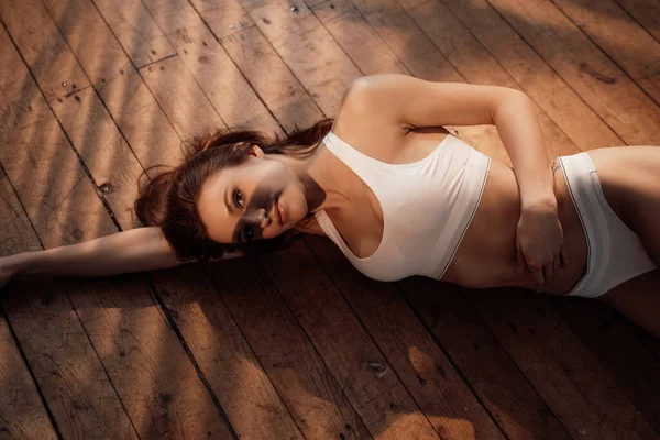 Photo of an almost nude female model posing while relaxing on wooden floor in apartment, wearing sporty underwear — Stock Photo, Image