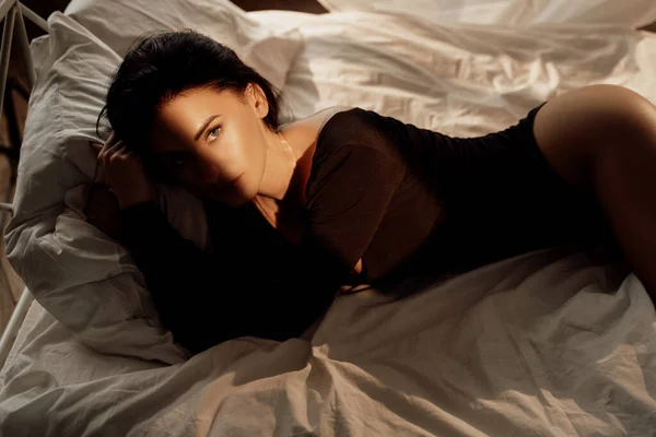 太陽の光の下で居心地の良いベッドに横たわっている間 黒体の衣装を身に着けている茶色の髪を持つ美しくセクシーな女性モデルの肖像画 — ストック写真