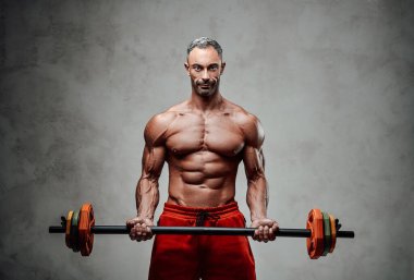 Atletik adam, beyaz beton arka planda izole edilmiş halterle biseps egzersizi yapıyor. Spor kıyafetler giyiyor, ciddi görünüyor.