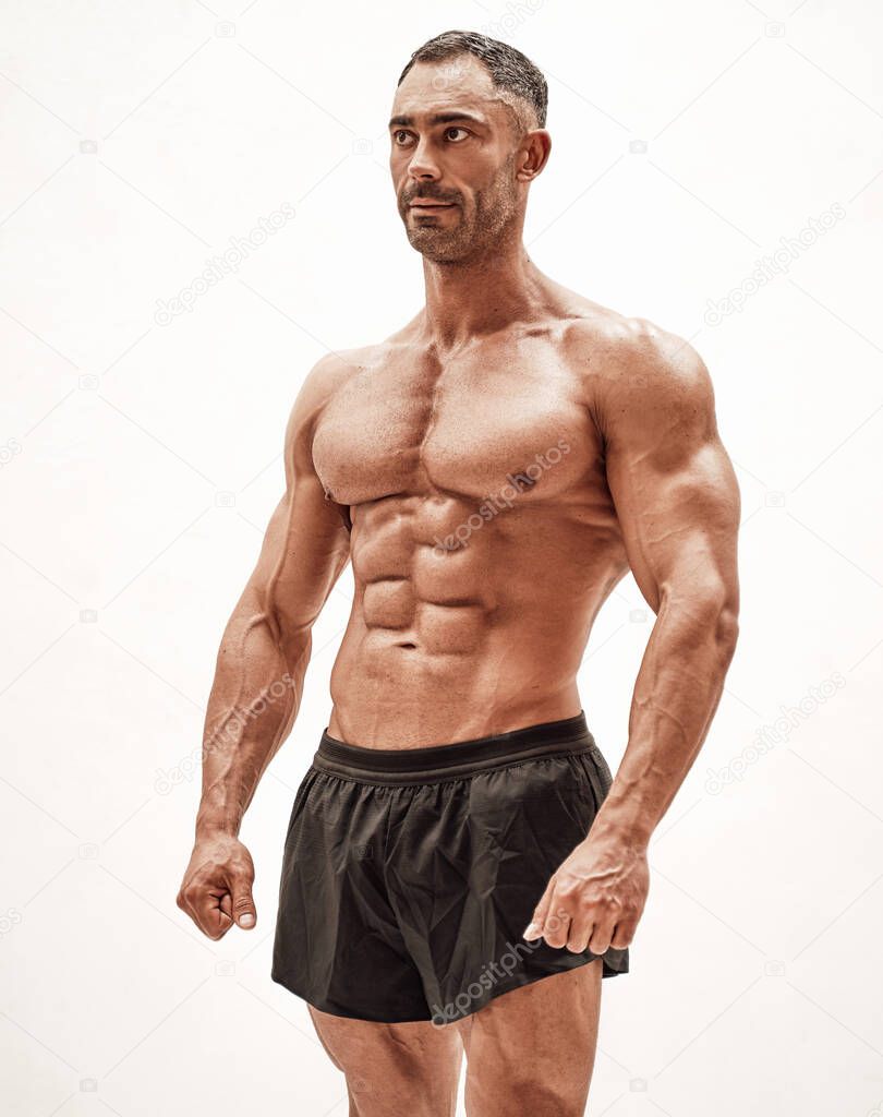 Masculine sportsman isolated on the white background wearing sport clothes showing his athletic body with naked torso, looking motivated