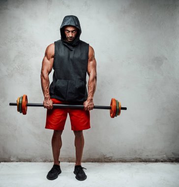 Parlak stüdyoda, halterle antreman yapmaya hazır, kırmızı şort ve kapüşonlu, uzun boylu bir fotoğrafla motive olmuş güçlü bir adam.