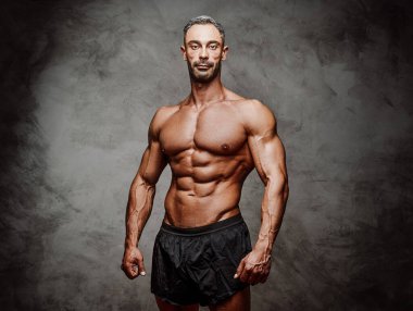 Gri beton arka planda izole edilmiş, spor şortlu, ciddi görünen bir fotoşop için poz veren atletik bir adam.