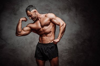 Parlak stüdyoda poz veren motive olmuş güçlü bir adam. Antrenmana başlayıp kaslarını göstermeye hazır.