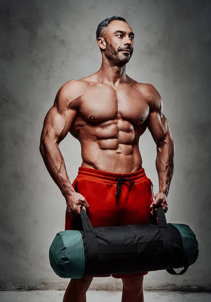 Brutaler Muskulöser Bodybuilder Der Mit Einem Gewichtsbeutel Vor Grauem Hintergrund — Stockfoto