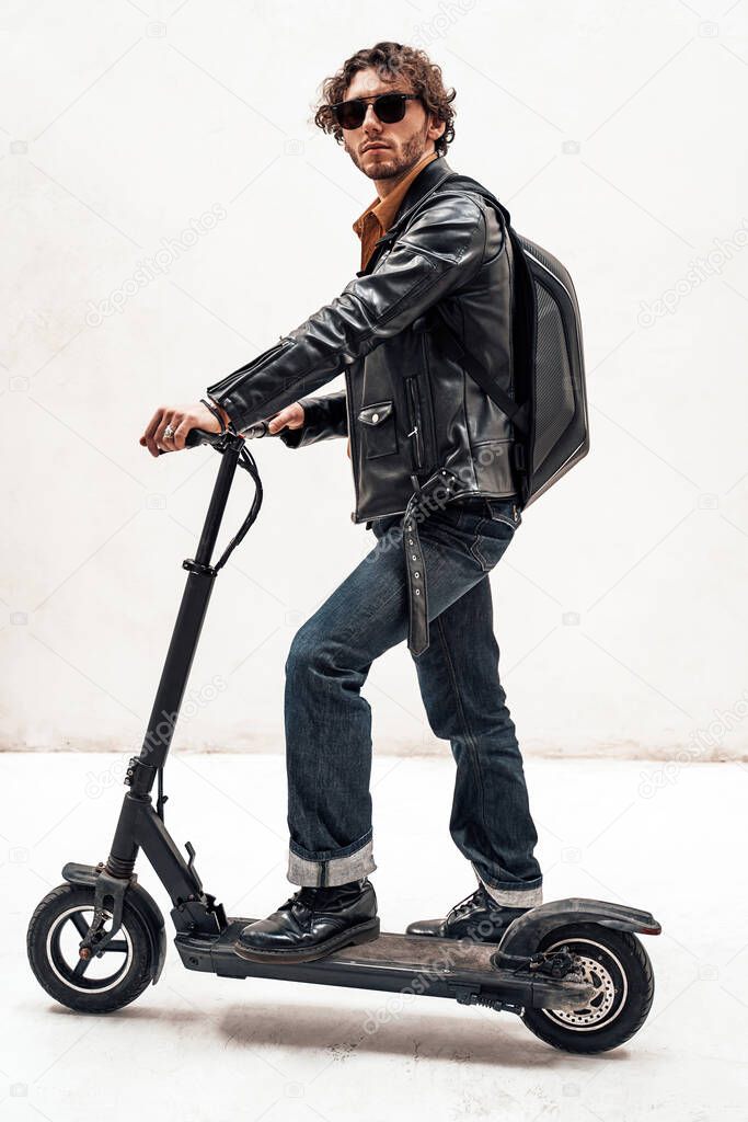 Assertive and rich young man posing on a scooter in a bright studio, looking cool