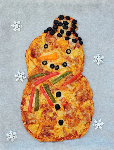 Christmas fun food idea for kids - snowman shaped pizza with pepperoni, pineapple, paprika, cheese and olives on white background, top view, flat lay