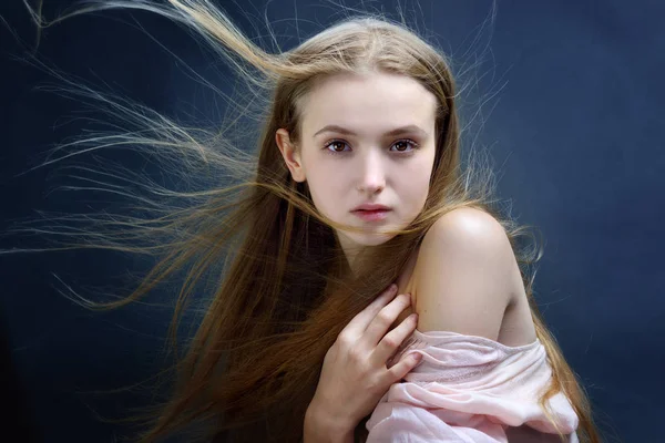 Portrait of the beautiful blonde woman with flying long hair. She is with naked shoulders  in studio .