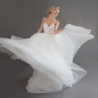 Lüks gelinlik içinde dans eden genç gelin. Güzel kız beyaz. Duygu mutluluk, kahkaha ve gülümseme, gri arka plan