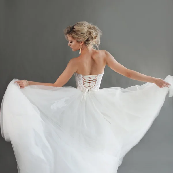 Tanzende junge Braut im luxuriösen Hochzeitskleid. hübsches Mädchen in Weiß. Glücksgefühle, Lachen und Lächeln, grauer Hintergrund — Stockfoto
