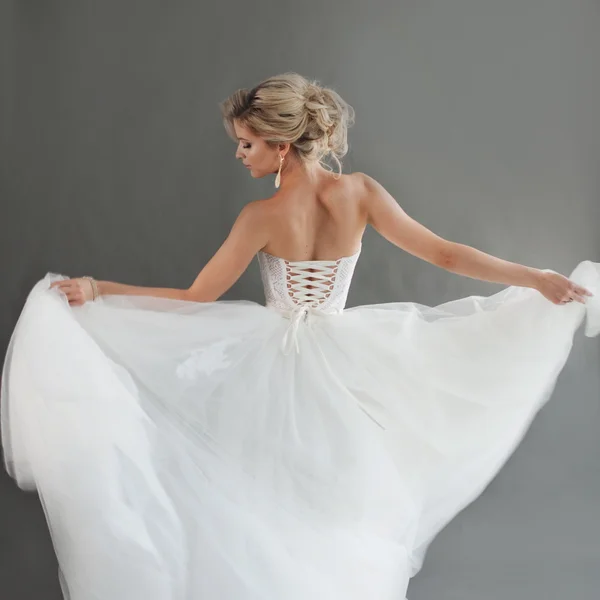 Bailando joven novia en lujoso vestido de novia. Una chica guapa de blanco. Emociones de felicidad, risa y sonrisa, fondo gris —  Fotos de Stock