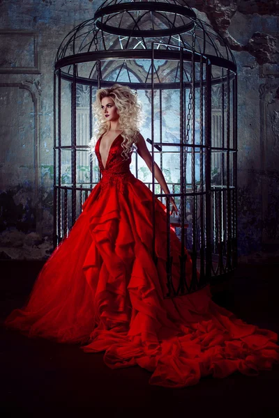 Mode blondin i röd klänning med fluffig kjol nära fågelbur, begreppet befrielse — Stockfoto
