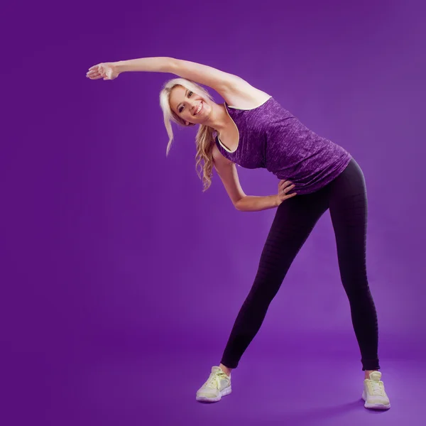 Menina bonita está envolvida em acrobacias. Estúdio fundo, roxo — Fotografia de Stock