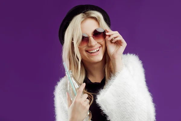 Jeune belle femme blonde au chapeau à la mode. Boire du soda à partir de bouteilles en verre. Joyeux et heureux — Photo