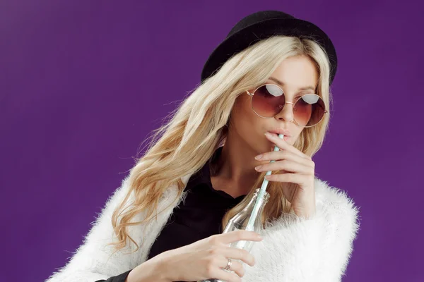 Jeune belle femme blonde au chapeau à la mode. Boire du soda à partir de bouteilles en verre. Joyeux et heureux — Photo