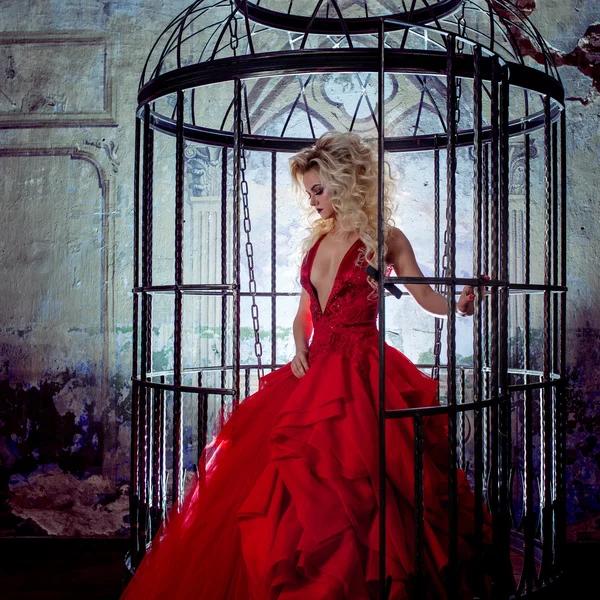 Mode blondin i röd klänning med fluffig kjol nära fågelbur, begreppet befrielse — Stockfoto
