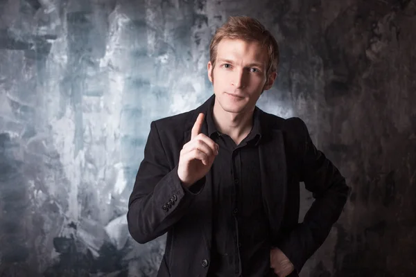 Young man conducts a dialogue in black suit on textured grey background — Stock Photo, Image