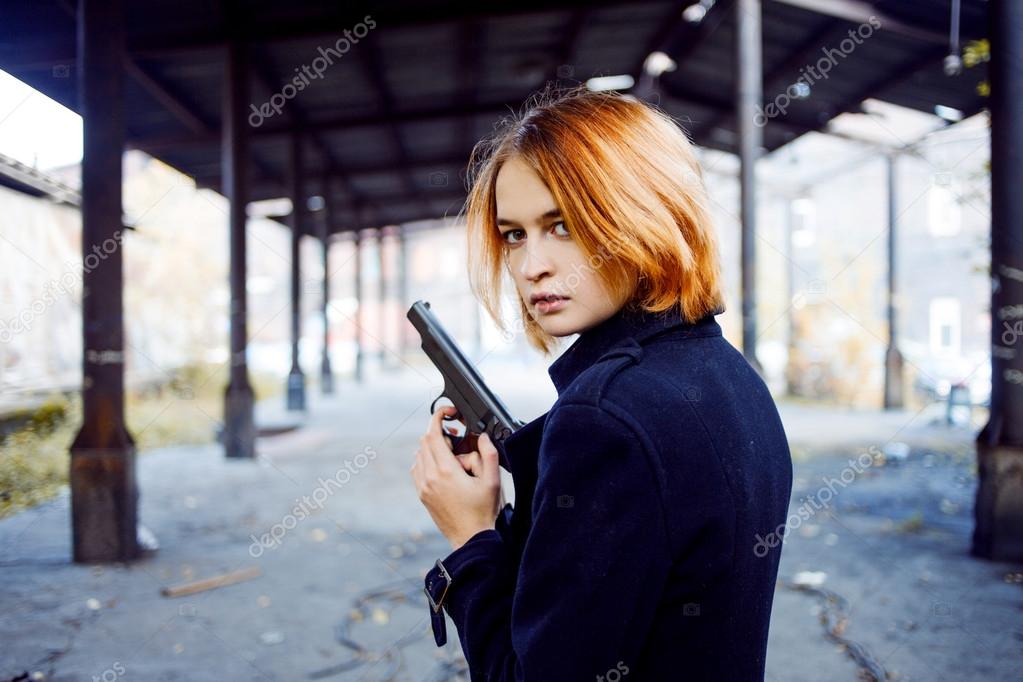 Woman pointing a gun. Mafia girl shooting at someone on the street.