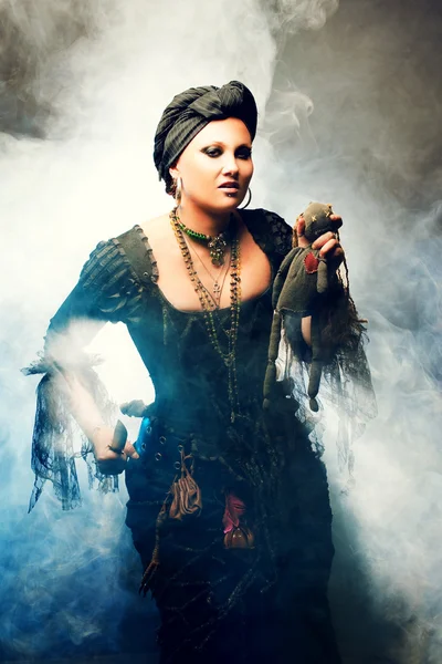 Bruja de Halloween crea magia. Mujer atractiva en traje de brujas con muñeca vudú en la mano —  Fotos de Stock
