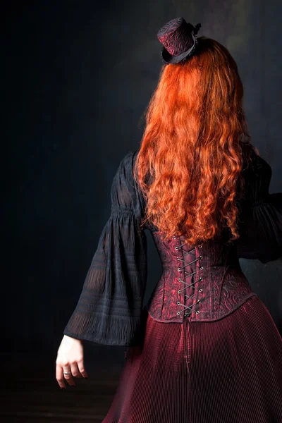 Hermosa mujer steampunk de vuelta. Chica esbelta de pelo rojo en corsé y sombrero —  Fotos de Stock