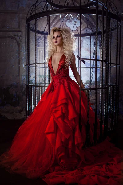 Moda loira em vestido vermelho com saia fofa perto da gaiola de pássaros, conceito de libertação — Fotografia de Stock