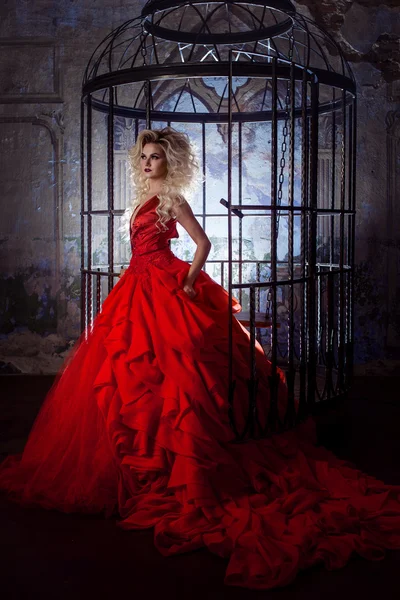Moda rubia en vestido rojo con falda esponjosa cerca de la jaula de los pájaros, concepto de liberación —  Fotos de Stock