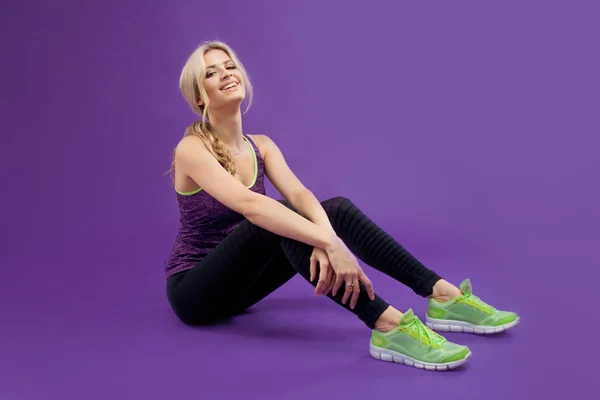 Beautiful young girl sitting on the floor and tying the laces of Shoe. Studio background, purple — Stock Photo, Image