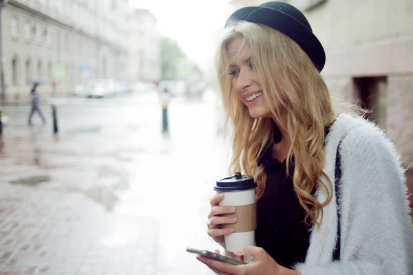 Mulher alegre na rua bebendo café da manhã e usar seu smartphone . — Fotografia de Stock