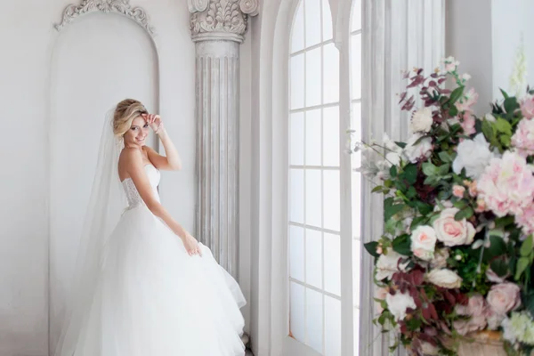 Encantadora joven novia en vestido de novia de lujo. Chica bonita, está cerca de la ventana grande — Foto de Stock