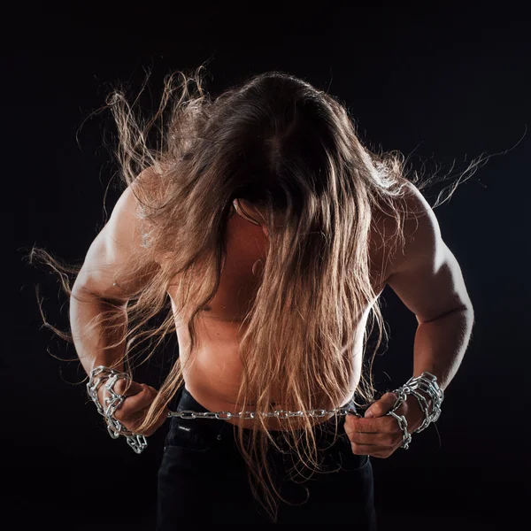 Ung man med långt hår bryter kedjan järn, lutade sig framåt. Stark. Begreppet motstånd — Stockfoto