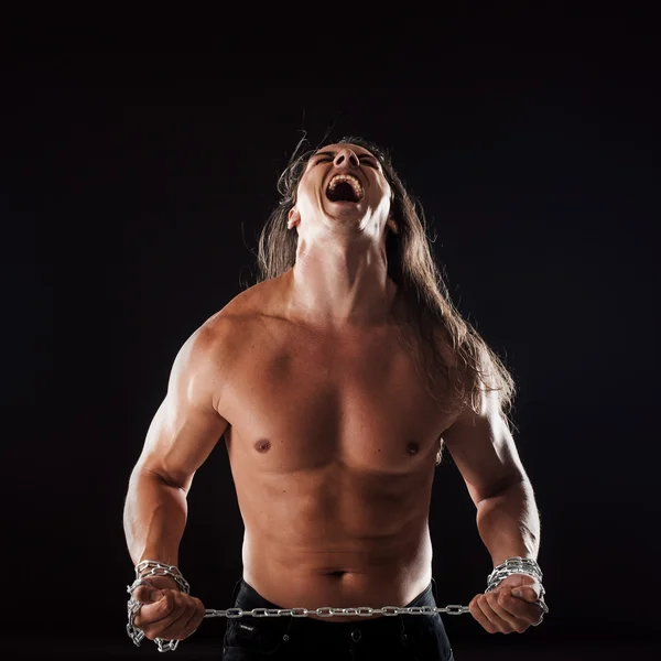Young man with long hair breaks the iron chain. Screaming his head thrown back. Concept of resistance — Stock Photo, Image