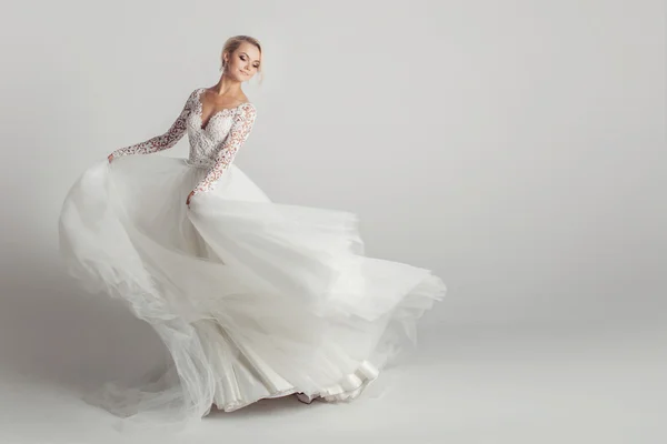 Beautiful attractive bride in wedding dress with long full skirt, white background, dance and smile — Stock Photo, Image