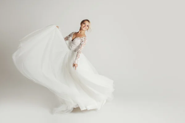 Hermosa novia atractiva en vestido de novia con falda larga y completa, fondo blanco, danza y sonrisa — Foto de Stock