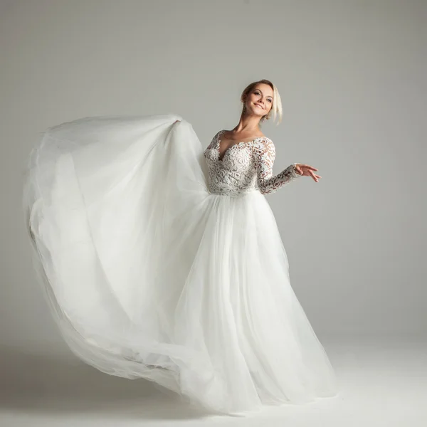 Привлекательная невеста в свадебном платье с длинной полной юбкой, белым фоном, танцами и улыбкой — стоковое фото