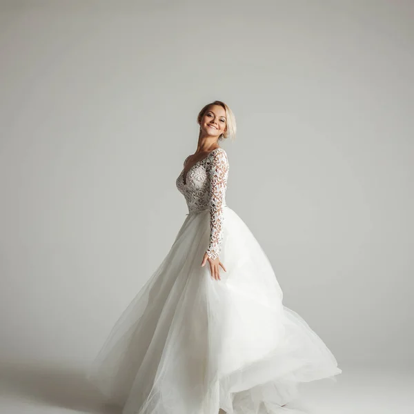 Beautiful attractive bride in wedding dress with long full skirt, white background, dance and smile — Stock Photo, Image