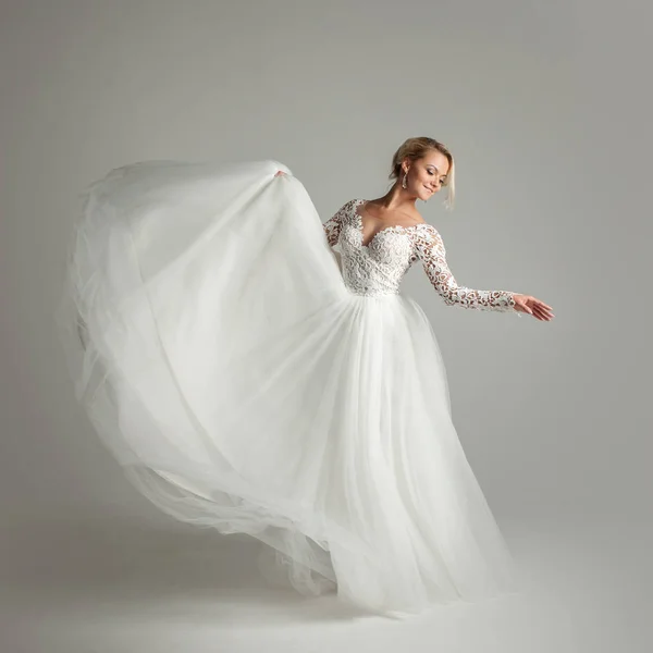 Mooie aantrekkelijke bruid in trouwjurk met lange volledige rok, witte achtergrond, dansen en lachen — Stockfoto