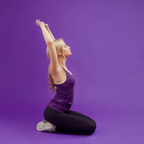 Postura de ioga. Jovens mulheres esportivas em um fundo roxo. Exala, puxa as mãos para cima — Fotografia de Stock