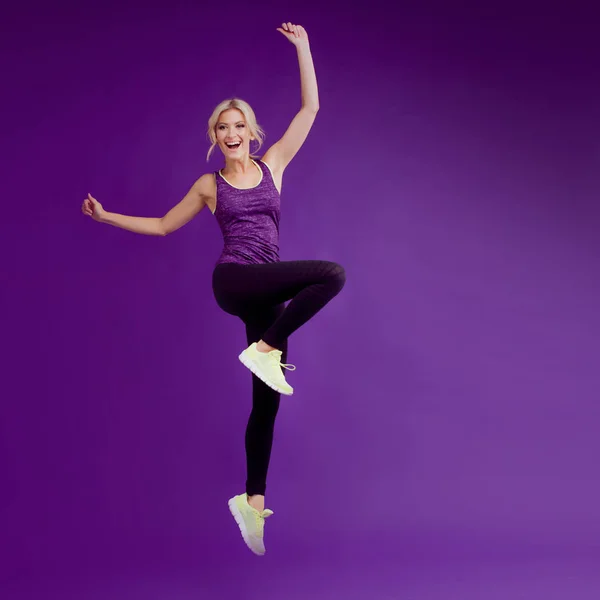 Hermosa joven en un corredor de pose. Fondo del estudio, morado. Feliz salto. — Foto de Stock