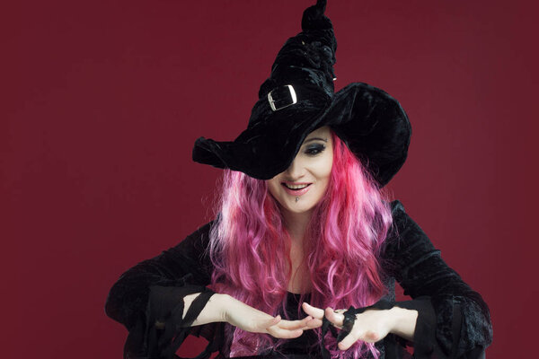 Привлекательная женщина в шляпе и костюме ведьмы с рыжими волосами выполняет магию над поверхностью зеркала, место для вашего текста или фотографии манипуляции
