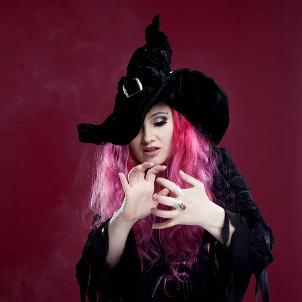 Attractive woman in witches hat and costume with red hair performs magic above the surface of the mirror, place for your text or photo manipulation — Stock Photo, Image