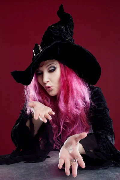 Attractive woman in witches hat and costume with red hair blows away something with hands, place for your text or photo manipulation — Stock Photo, Image