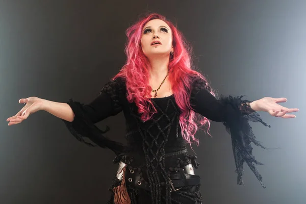 Хэллоуинская ведьма творит магию. Привлекательная женщина с рыжими волосами в костюме ведьмы, вытянутые руки, сильный ветер — стоковое фото