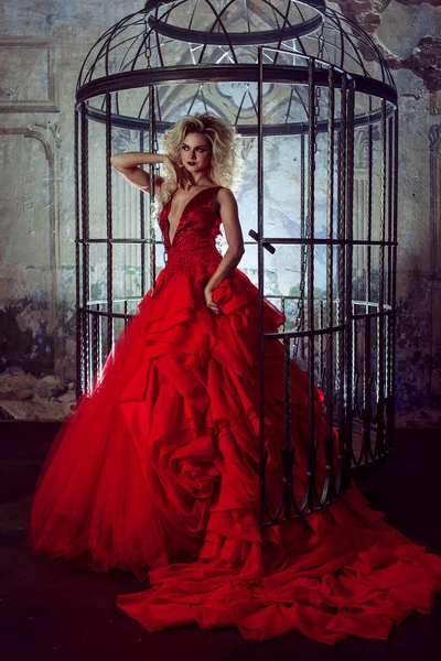 Fashion blonde in red dress with fluffy skirt near the birdcage, concept of liberation — Stock Photo, Image