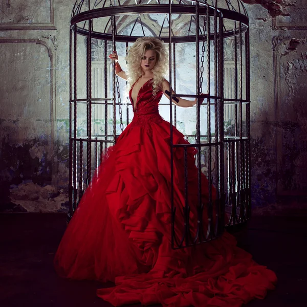 Fashion blonde in red dress with fluffy skirt near the birdcage, concept of liberation — Stock Photo, Image