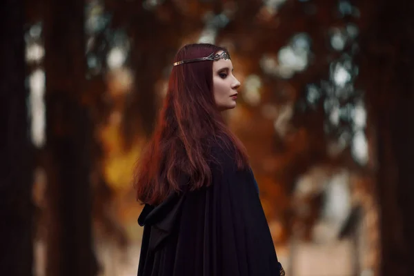 Jeune femme belle et mystérieuse dans les bois, en manteau noir avec capuche, image d'elfe de forêt ou de sorcière — Photo