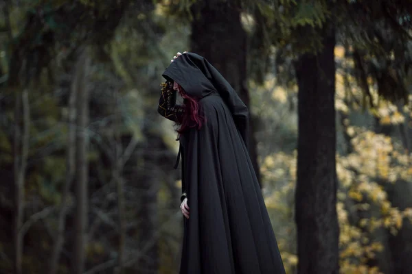 Jovem mulher bonita e misteriosa na floresta, em manto preto com capuz, imagem de elfo da floresta ou bruxa — Fotografia de Stock