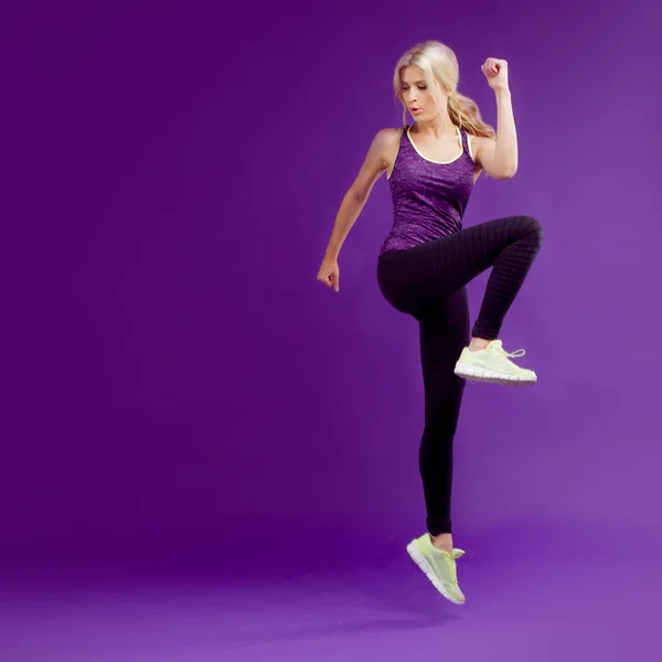 Beautiful young girl in a pose runner. Studio background, purple. Happy jumping — Stock Photo, Image