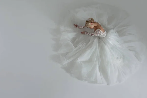 美丽的新娘，在奢华的婚礼礼服，裙子躺在附近，一个圆的形状。白色背景，顶视图 — 图库照片