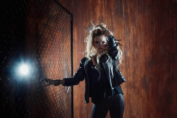 Rocknroll girl, young beautiful woman dances in dark alley, against the fence mesh — Stock Photo, Image