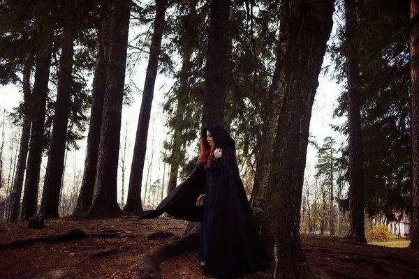 Jeune femme belle et mystérieuse dans les bois, en manteau noir avec capuche, image d'elfe de forêt ou de sorcière — Photo