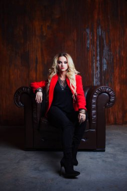 Genç ve çekici sarışın kadın kırmızı ceketli oturur deri koltuk, arka plan grunge paslı duvar